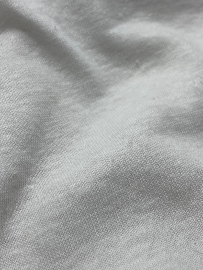 May include: Close-up of a white fabric with a textured surface. The fabric is soft and has a slightly wrinkled appearance.