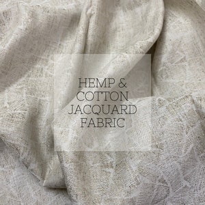 Peut inclure: Gros plan sur un tissu jacquard en chanvre et coton plié. Le tissu a un aspect texturé et tissé avec une palette de couleurs neutres beige et blanc cassé. Le texte "HEMP & COTTON JACQUARD FABRIC" est superposé.