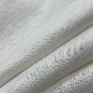 May include: Close-up of a white fabric with a soft, textured surface. The fabric is folded and shows the weave of the material.