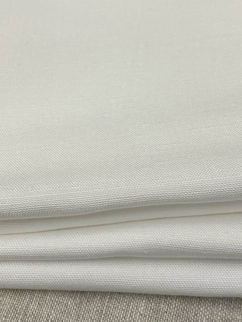 May include: White fabric with a smooth, woven texture. The fabric is folded in thirds, showing the texture and color.
