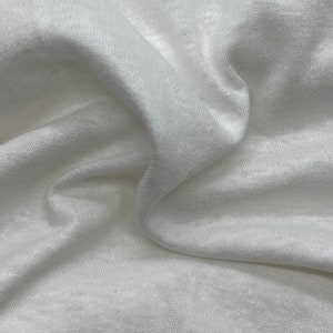 May include: White fabric with a soft, textured surface. The fabric is wrinkled and folded, showing its drape and texture.