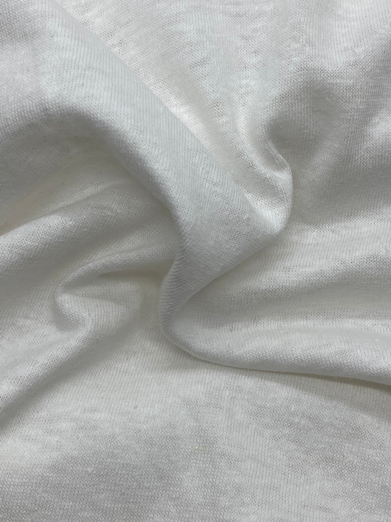 May include: White fabric with a soft, textured surface. The fabric is wrinkled and folded, showing its drape and texture.