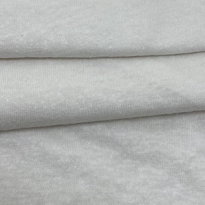 May include: Close-up of a white fabric with a textured surface. The fabric is folded in thirds, showing the texture and weave.