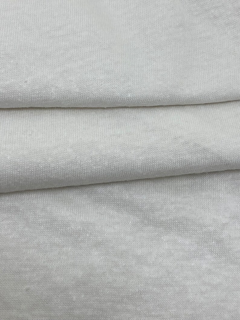 May include: Close-up of a white fabric with a textured surface. The fabric is folded in thirds, showing the texture and weave.