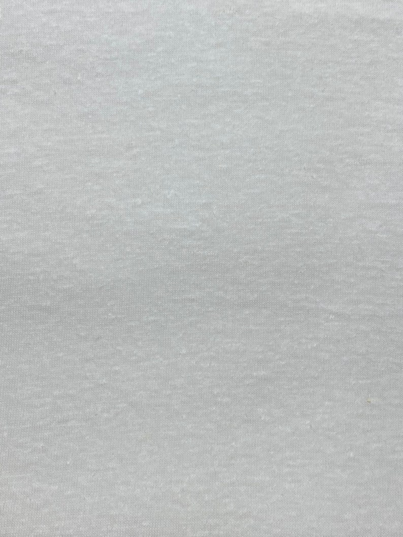 May include: A close-up of a light gray fabric with a subtle texture. The fabric has a smooth, even surface with a slightly grainy appearance.