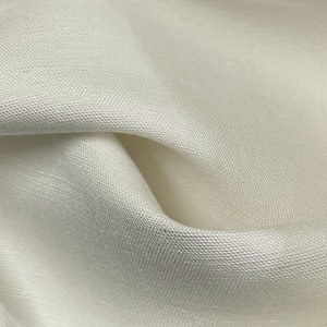 May include: Close-up of a white fabric with a subtle textured weave. The fabric is soft and smooth, with a slight sheen.