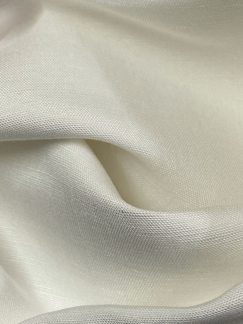 May include: Close-up of a white fabric with a subtle textured weave. The fabric is soft and smooth, with a slight sheen.