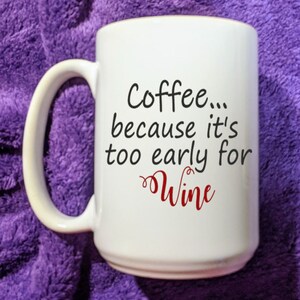 May include: White ceramic coffee mug with a black and red design. The mug reads "Coffee... because it's too early for wine".