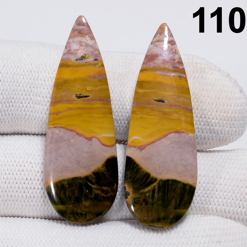 May include: Two polished, teardrop-shaped gemstones. The stones feature a blend of colors, including yellow, pink, and dark green, with a layered, natural pattern. The number "110" is visible in the upper right corner. These stones are suitable for jewelry making.