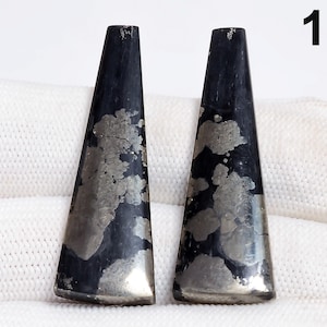 May include: Two dark, elongated, trapezoid-shaped stones with a metallic, silver-gray pattern. The stones are set against a white background. The number "1" is in the upper right corner.