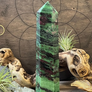 Może przedstawiać: Zielona, czarna i różowa wieża z kamienia szlachetnego ze spiczastym wierzchołkiem. Wieża stoi na drewnianej powierzchni z ozdobnym wzorem koła.