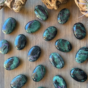 Może przedstawiać: Kolekcja 17 gładkich, owalnych, zielonych i czarnych kamieni szlachetnych, które zostały obrobione w sposób przypominający kamienie szlifowane. Kamienie mają różne zielone i czarne wzory i wiry.