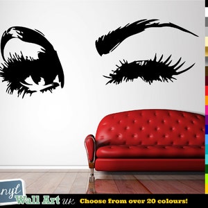 Könnte beinhalten: Schwarz-weiß Wandtattoo eines Frauenauges mit Wimpern und Augenbraue. Das Tattoo befindet sich an einer weißen Wand mit einem roten Sofa im Vordergrund. Wählen Sie aus über 20 Farben!