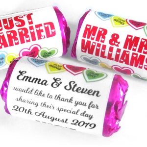 May include: Three cylindrical candy bars wrapped in bright pink foil with white labels. One label reads JUST MARRIED, another MR & MRS WILLIAMS, and the third Emma & Steven would like to thank you for sharing their special day 20th August 2019.