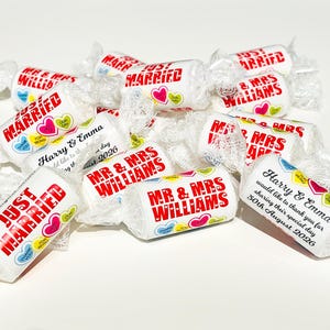 May include: A collection of white cylindrical candies wrapped in clear plastic. The wrappers feature red text reading "JUST MARRIED" or "MR & MRS WILLIAMS" alongside colorful heart graphics with "THANK YOU" and "FOR BEING" printed inside.