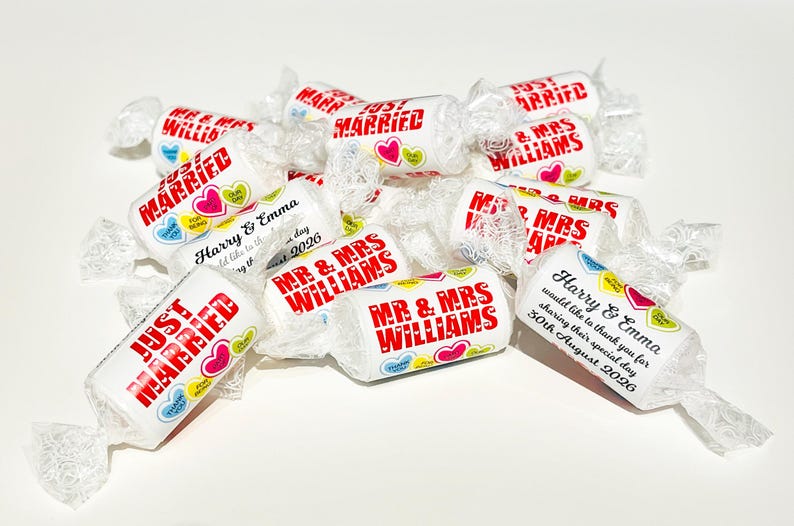 May include: A collection of white cylindrical candies wrapped in clear plastic. The wrappers feature red text reading "JUST MARRIED" or "MR & MRS WILLIAMS" alongside colorful heart graphics with "THANK YOU" and "FOR BEING" printed inside.