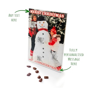 May include: A Christmas advent calendar featuring a snowman design with a family photo. The calendar has small doors with chocolate inside. The text "MERRY CHRISTMAS" and "...A HAPPY NEW YEAR!" are printed on the calendar.