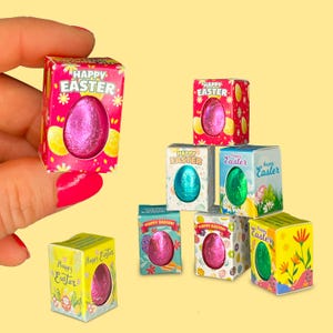 May include: Assortment of small boxes with colorful Easter egg designs. Each box contains a foil-wrapped chocolate egg. The boxes have the text "Happy Easter" on them.