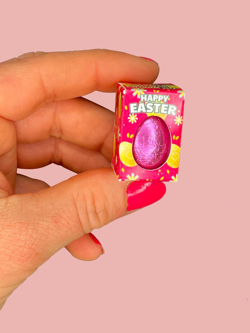 May include: A small pink box with a pink and white floral design. The box says "Happy Easter" and contains a pink foil-wrapped chocolate egg.