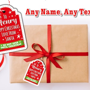May include: Red and green Christmas gift tag with white border and white text that reads "To Henry Happy Christmas Love From Santa Do Not Open Until Christmas". The tag is tied to a brown gift box with a red ribbon.