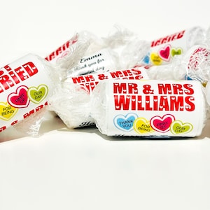 May include: A collection of white individually wrapped candies featuring red text that reads JUST MARRIED and MR & MRS WILLIAMS. The wrappers include colorful heart graphics with text that reads THANK YOU, FOR BEING, PART OF, OUR DAY.