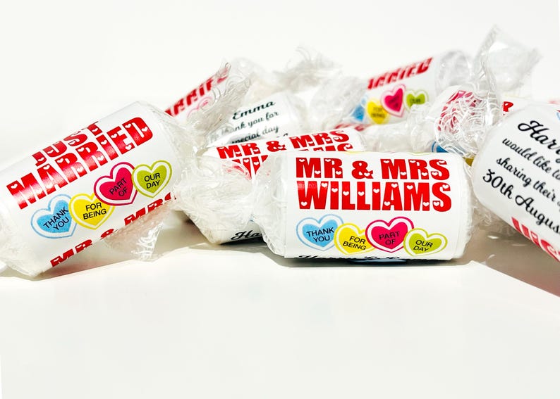 May include: A collection of white individually wrapped candies featuring red text that reads JUST MARRIED and MR & MRS WILLIAMS. The wrappers include colorful heart graphics with text that reads THANK YOU, FOR BEING, PART OF, OUR DAY.
