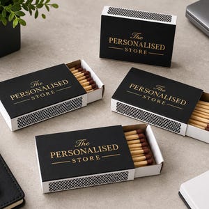 May include: Four rectangular matchboxes with black covers and gold text reading The Personalised Store. Three boxes are partially open, revealing wooden matches with dark brown tips. The sides of the boxes feature a white and black honeycomb pattern.