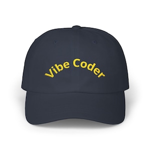 May include: Navy blue baseball cap featuring the embroidered text "Vibe Coder" in yellow. The cap has a curved peak and a structured fit. A casual accessory.