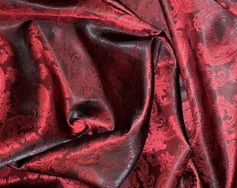 May include: Red paisley patterned fabric with a satin sheen. The fabric is draped and folded, creating a textured look.