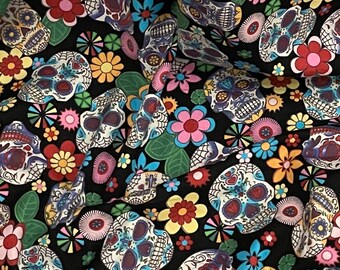 May include: A black fabric with a repeating pattern of colorful sugar skulls and flowers. The skulls are white with black outlines and have colorful details. The flowers are in various colors, including pink, yellow, blue, and red.