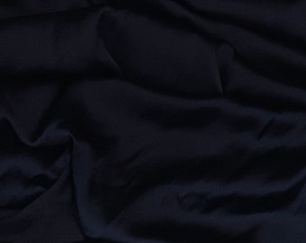 May include: A dark blue fabric with a smooth, silky texture. The fabric is draped and folded, creating soft, flowing lines.