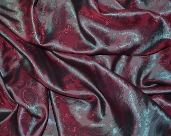 May include: Close-up of a burgundy fabric with a paisley pattern. The fabric has a subtle sheen and is draped in soft folds.
