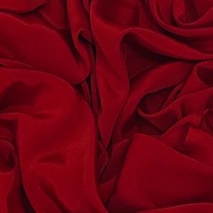 Pode incluir: Um close-up de um tecido vermelho escuro com dobras suaves e fluidas.