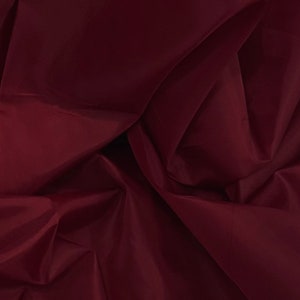 May include: A close-up of a deep burgundy fabric with soft, flowing folds. The fabric has a smooth, silky texture.