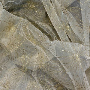 May include: White sheer fabric with a gold glitter pattern of stylised flowers. The fabric is draped and textured.