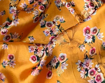 May include: A close-up of a fabric with a floral pattern. The fabric is a light orange color with a variety of pink, white, and purple flowers. The fabric is soft and silky.