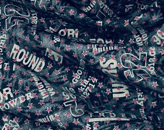 May include: Dark fabric with a repeating pattern of white text and small red stars. The text includes words like "ROUND", "POWER", and numbers. The fabric appears to be draped, creating shadows and texture.