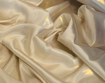 May include: Close-up of a smooth, white fabric with a subtle sheen. The fabric is draped and folded, creating soft, flowing lines.