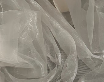 May include: White sheer fabric with a delicate, shimmering texture. The fabric is draped and folded, creating soft, flowing lines.