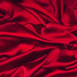 Pode incluir: Close-up de um tecido de cetim vermelho escuro com dobras suaves e fluidas e uma textura luxuosa.