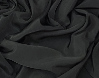 May include: Close-up of a black fabric with a smooth, silky texture. The fabric is draped and folded, creating soft, flowing lines.
