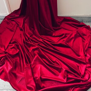 Puede incluir: Una tela de terciopelo rojo oscuro drapeada sobre un suelo de madera. La tela es lisa y tiene un ligero brillo.