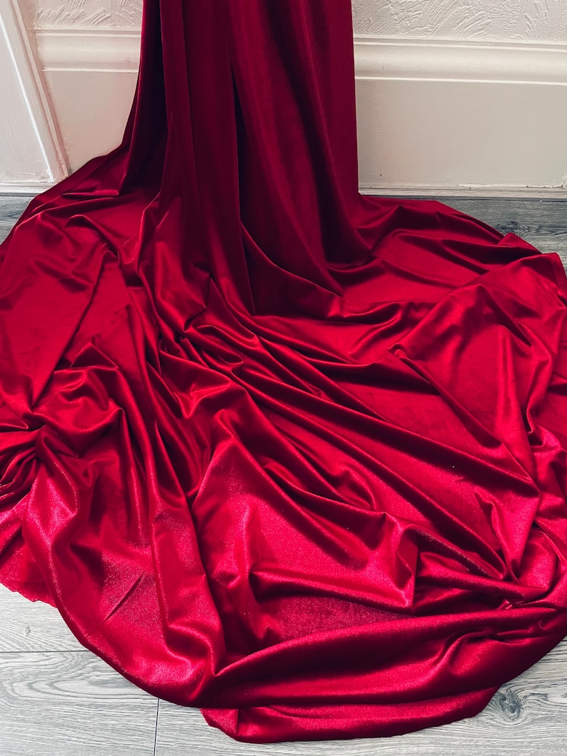 Puede incluir: Una tela de terciopelo rojo oscuro drapeada sobre un suelo de madera. La tela es lisa y tiene un ligero brillo.