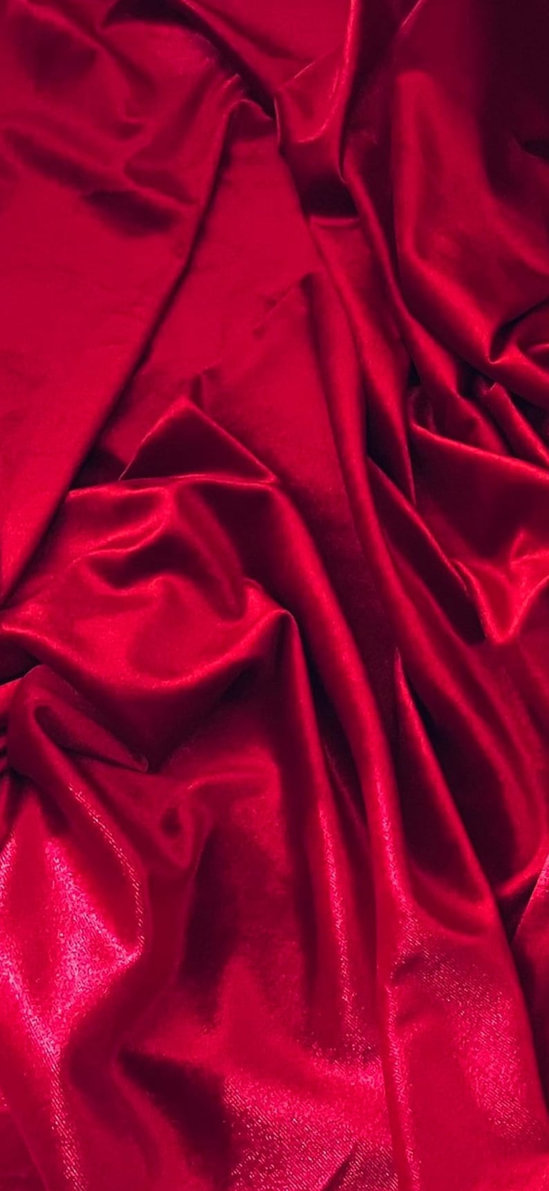 Puede incluir: Primer plano de una tela de terciopelo rojo intenso con pliegues suaves y fluidos y un brillo sutil.