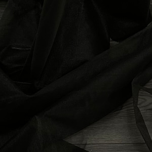 Può includere: Tessuto nero trasparente drappeggiato su una superficie scura. Il tessuto è morbido e fluido, creando un look drammatico ed elegante.