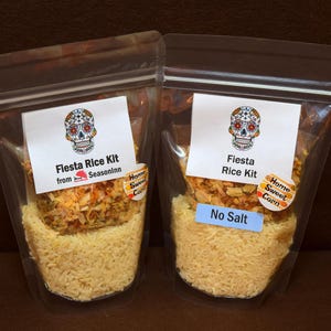 May include: Two clear plastic bags filled with Fiesta Rice Kit. Each bag has a white label with a sugar skull design and the text "Fiesta Rice Kit". One bag has a blue "No Salt" sticker.