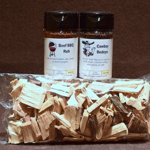 May include: Two spice jars labeled "Beef BBQ Rub" and "Cowboy Redeye" with illustrations. A clear bag of wood chips sits in front. The BBQ rub is for beef brisket, ribs, steak, or burgers. The Cowboy Redeye is for beef, bison, chicken wings, wild game, or chili.
