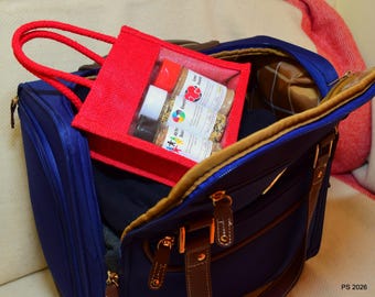 Könnte beinhalten: Eine kleine rote Jute-Tragetasche mit einem durchsichtigen Kunststofffenster, das drei Gewürzgläser mit weißen Etiketten enthält. Die Tasche befindet sich in einer großen marineblauen Reisetasche mit braunen Lederakzenten.
