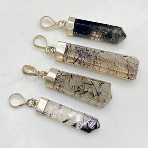 以下が含まれることがあります： 銀色の金属製のキャップとループが付いた、長方形のクリスタルペンダント4つ。クリスタルは黒、クリア、スモーキーな色合いで、色合いが異なります。各ペンダントには、黒いインクルージョンのユニークなパターンがあります。