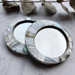May include: Two round, white, decorative mirrors with iridescent mother of pearl inlays. The mirrors are approximately 7.5 cm in diameter.